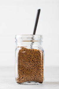 Glass jar with instant coffee with a spoon on a light background.