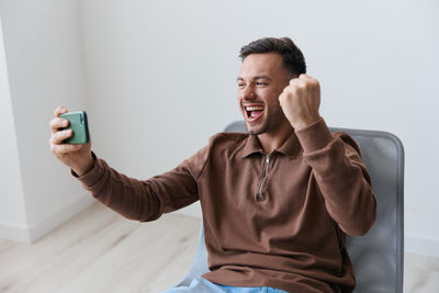 Young man using mobile phone while standing against wall