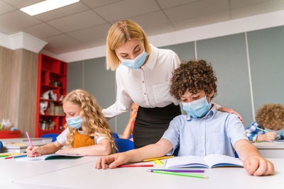 Teacher wearing mask teaching student at classroom