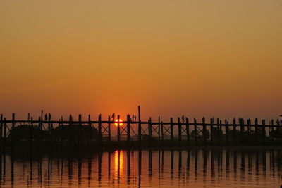 Silhouette bridge over sea against orange sky