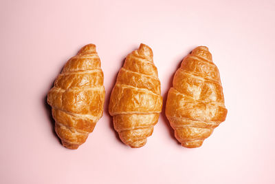 Three fresh-baked crispy golden buttery croissants isolated on pink background with copy space.