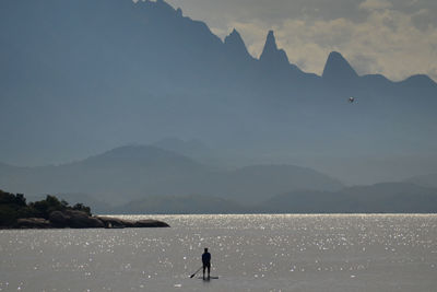Man paddleboarding in sea against mountains