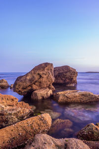 Rocks on sea shore against clear blue sky
