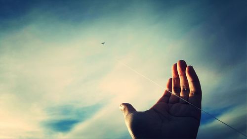 Cropped hand flying kite against cloudy sky