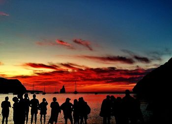 Silhouette people on beach against orange sky