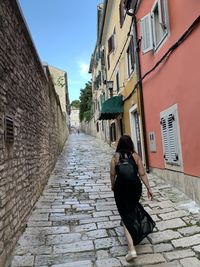 Rear view of woman walking on footpath by buildings