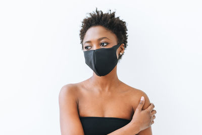 Beautiful young african american woman in black top and face mask on white, stop coronavirus concept