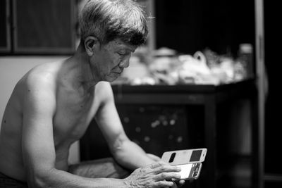 Shirtless senior man using phone while sitting at home
