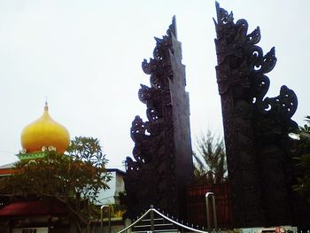 Low angle view of cross amidst buildings against clear sky