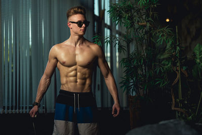 Shirtless muscular man standing against window at home