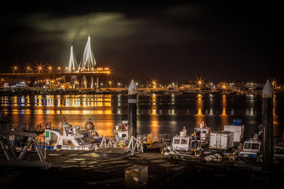 Illuminated boats moored in river against sky at night