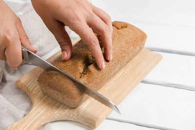 Woman hands holding knife and cutting sourdough homemade bread on cutting board on white table