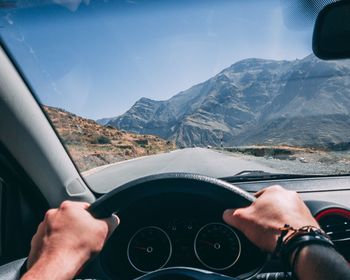 Cropped hands of man driving car on road against sky