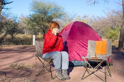 Female tourist having drink while sitting on campsite