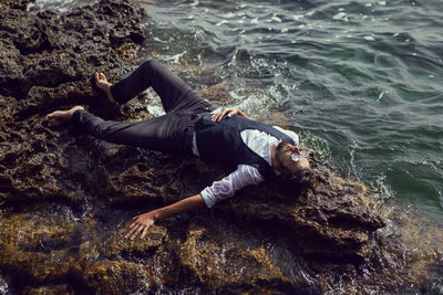 Man with a beard in dark clothes and a white shirt sits on the stone seashore in  crimea tarkhankut