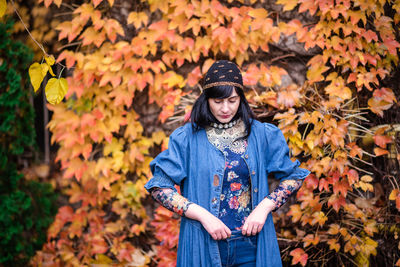 Portrait of young woman standing by maple leaves during autumn