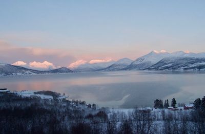 Scenic view of lake by snowcapped mountains against sky during sunset