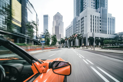 Cars on road by buildings against sky in city