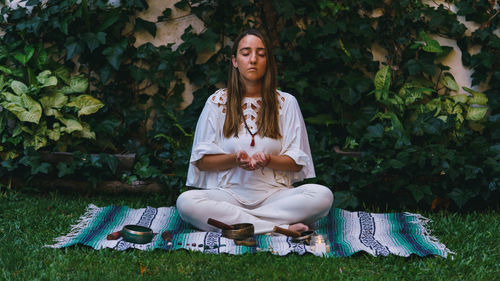 Full length of young woman meditating while sitting outdoors