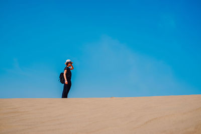 Full length of woman standing on desert against blue sky