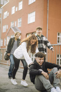 Teenage girl pushing male friend sitting on skateboard