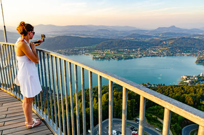 Woman with monopod standing by railing while looking at view