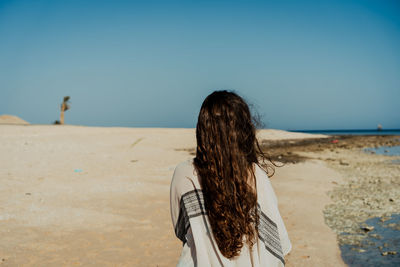 Rear view of woman standing at beach against clear sky