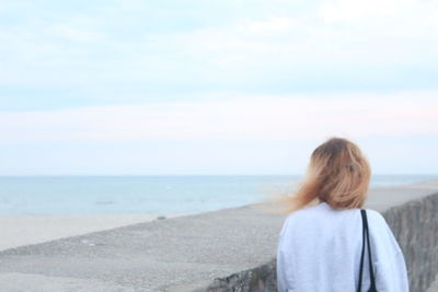 Rear view of woman standing on beach against sky