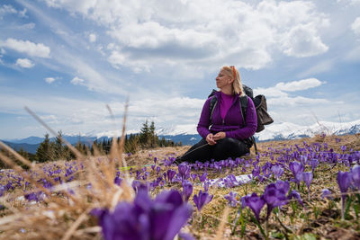 Side view of woman standing amidst flowering plants on field against sky