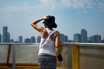 Rear view of woman standing by railing against cityscape