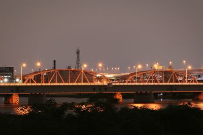 Illuminated bridge over river against sky at night