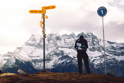 Rear view of male hiker standing on field by information sign during winter