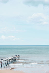 Distant seaside beach scene of people walking on a pier stretching out over the sea on a sunny day.