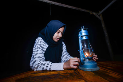 Portrait of young woman standing against black background