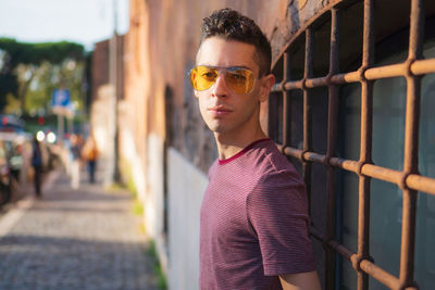 Portrait of young man wearing sunglasses while standing against wall