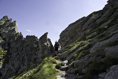 Rear view of man walking on rocks against sky