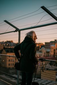 Man standing by railing against sky during sunset