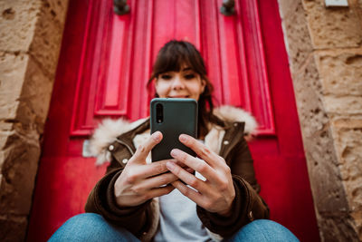 Close-up of woman using smart phone while sitting by door