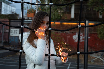 Young woman with illuminated string lights holding ropes of jungle gym