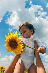 Mother holding boy with sunflower at field against sky