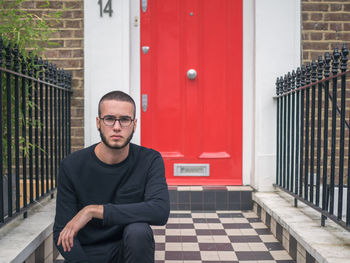 Portrait of man sitting against red door