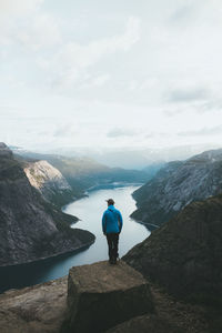 Rear view of man standing on cliff with valley in background against sky