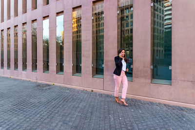 Full length of woman standing on footpath by building