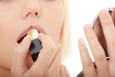 Midsection of woman applying lipstick against white background