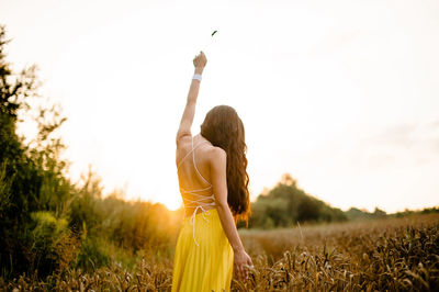 A girl runs through a field with spikelets against the background of the setting sun