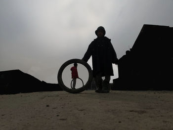 Silhouette man standing on bicycle at beach against sky