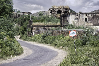 Road sign by trees against sky in city in bhangarh fort, rajasthan 