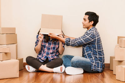 Man putting box on girlfriend while sitting on floor at new home