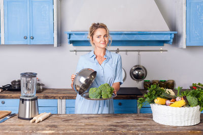 Beautiful woman holding broccoli standing in kitchen