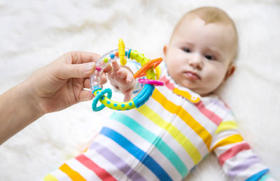 Mother holding toy while baby lying on bed